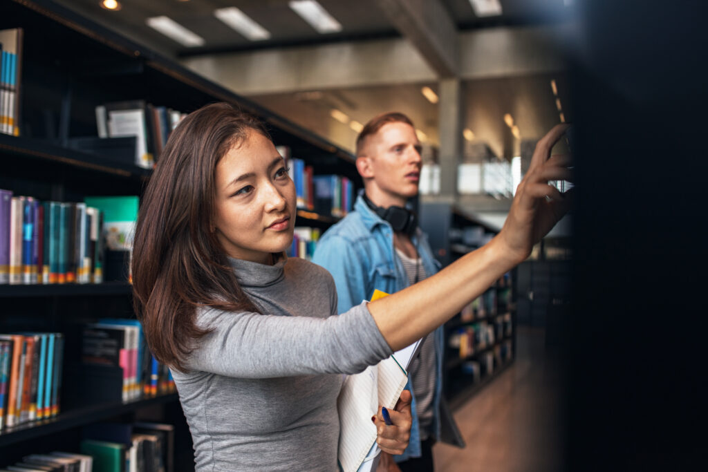 university students taking book from shelf in library